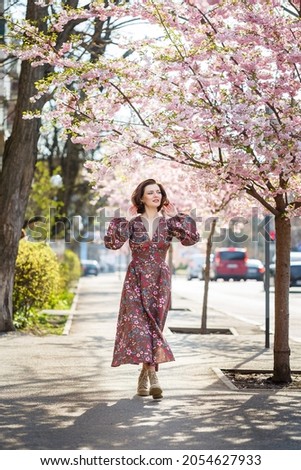 Beautiful young woman in a dress in blooming sakura trees. It's a spring warm sunny day outside