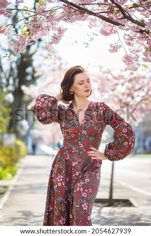 Beautiful young woman in a dress in blooming sakura trees. It's a spring warm sunny day outside
