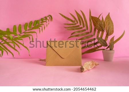 The composition features summer products. greeting card on logs on pink background with dried leaves decoration.
