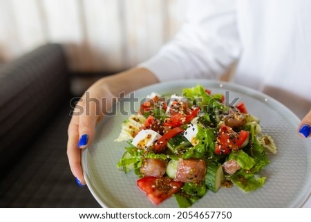 The young female waiter holding in her hands the plate with the Greek salad.