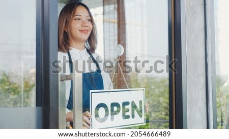 Happy Asian beautiful young woman staff turning round sign to open on door, Female owner of coffee shop opening the service after lockdown quarantine, new normal reopening