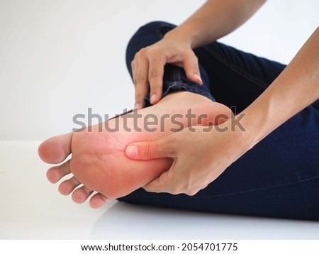 Pain in the foot, woman holds her hands to her feet, foot massage, cramp, muscular spasm, red accent on foot on white background.
