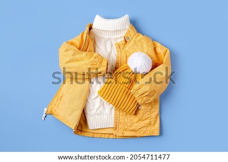 Yellow jacket and warm sweater and hat on blue background. Set of children's clothes for autumn or winter. Fashion kids outfit.
