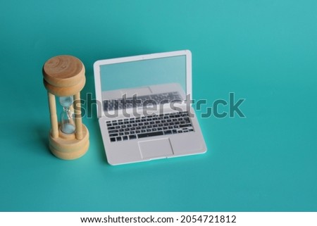 Selective focus image of hourglass and laptop on green background. Screen time limits concept. 