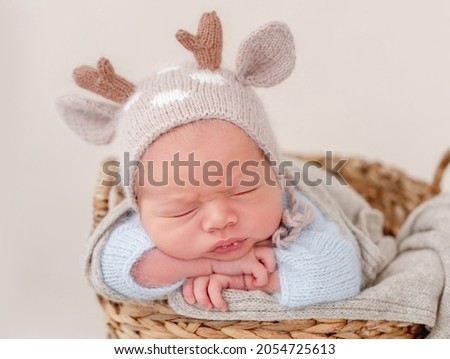 Portrait of newborn baby boy wearing knitted hat with deer horns sleeping on his tummy and holding tiny hands under his cheeks. Adorable infant child napping
