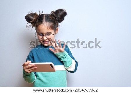 Happy cute little girl isolated on white studio background with mobile phone in hands, child holding smartphone smiling laughing