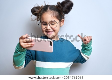 Happy cute little girl isolated on white studio background with mobile phone in hands, child holding smartphone smiling laughing
