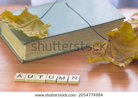 old closed book, autumn maple foliage, inscription autumn in wooden letters on the table. Autumn mood theme. selective focus, shallow depth of field