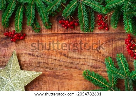 Christmas background. Spruce branches, red berries, golden star on a wooden background. Copy space, frame, place for text. Top view. Christmas or New Year's card. flat lay