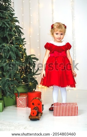 Embarrassed girl near the Christmas tree with gifts and a toy train of Christmas lights and festive tree