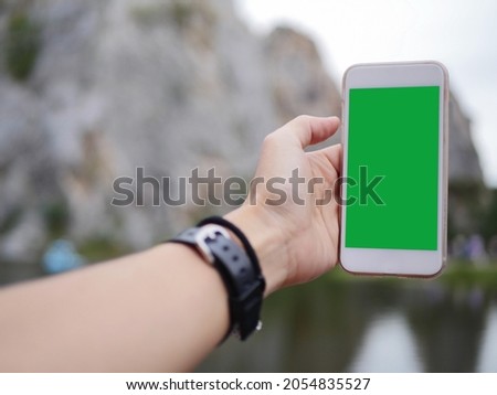 Mobile phone in the hand with green colour screen to show at the mountain background 