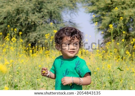 Close-up portrait of An Indian little child playing in a field with yellow mustard flowers, india