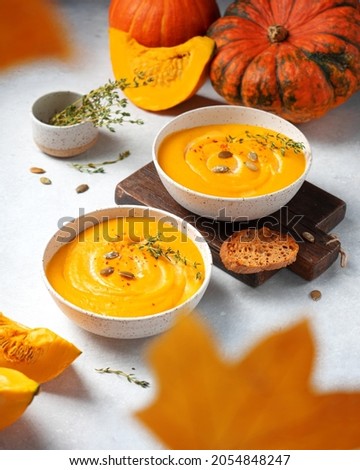 Two bowls of pumpkin cream soup with croutons and pumpkin seeds. Side view. Сomposition with autumn leaves