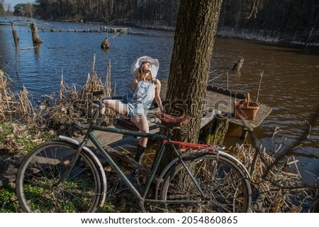 A girl in denim shorts and an old bicycle by the lake on a warm summer day in the evening sunlight.