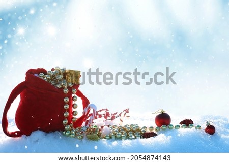 Winter Holidays background with red santa bag. Christmas balls and gift box on snow. New Year greeting card  with fir tree branch.