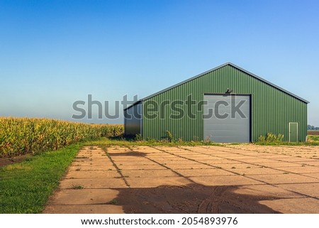 Modern agricultural barn with a yard of concrete slabs. The photo was taken in the Netherlands on a sunny day in the fall season. Royalty-Free Stock Photo #2054893976