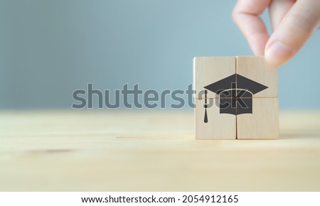 Graduation from university, education, diploma concept. Happiness cheerful feeling, Commencement, Graduation day. Hand hold wooden cube with graduation cap on beautiful grey background and copy space.