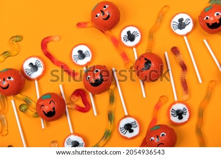 Halloween candy with black spiders,cobweb,smiling pumpkins  and tasty jelly worms on orange color background,top view