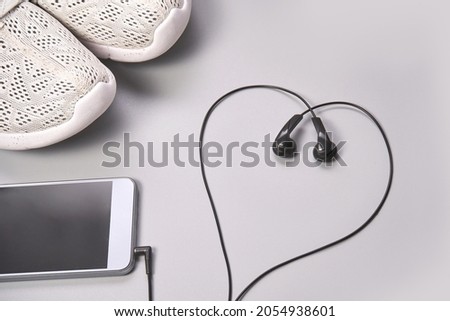 Listen podcast at running training. Black earphones heart shape. Grey background. Storylines jogging. Sport lifestyle concept. Gym sneakers audio playlist