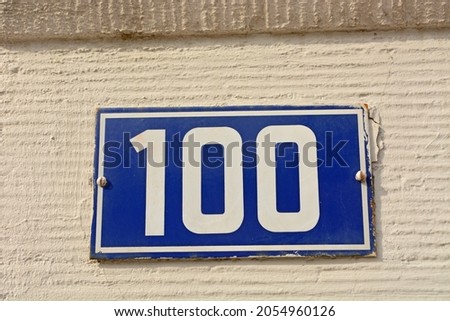 A blue house number plaque, showing the number hundred (100) 