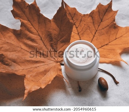 white jar with oily cream for cold weather against a background of red maple leaves
