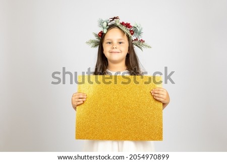 close-up portrait of charming, smiling girl in Christmas wreath holding golden, shiny blank banner isolated on white background. 