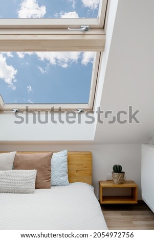 Concept of morning light in house. Vertical view of clean skylight in white bedroom interior. Modern apartment with attic window in small room with home decor, green house plants and cushions on bed Royalty-Free Stock Photo #2054972756