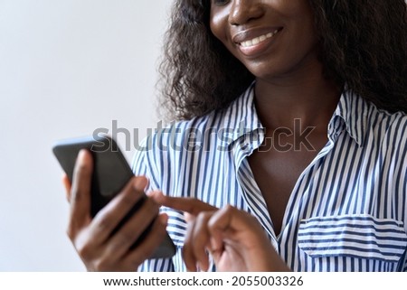 Young smiling black African woman holding smartphone in hand looking at cell phone device using mobile application technology for texting, banking, money transfer or shopping online. Close up view