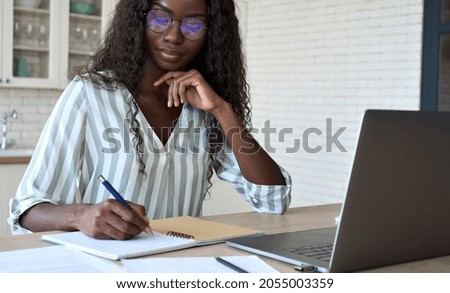 Young black African woman student learning online using laptop computer, taking notes, watching webinar or virtual education remote e class studying at home. Distance education concept.