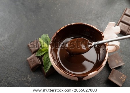 Pastry chef mixes hot chocolate with spoon in bowl, top view with mint leaves. recipe Cooking handmade chocolate bar, dessert, candies. Confectionery covered with chocolate topping with mints leaf
