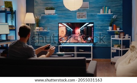 Caucasian gamer playing action games on tv console using wireless joystick with modern technology. Young man of simulator enjoyment gaming on electronic devices as hobby and leisure