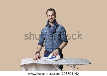 Portrait of a happy young man ironing shirt over colored background