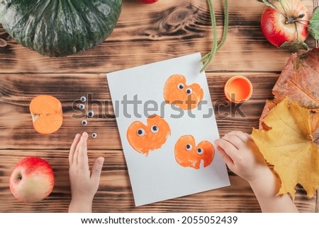 Step-by-step Halloween childrens tutorial pumpkin apple prints. Step 12: Child hand glues eyes to all pumpkin prints. Top view