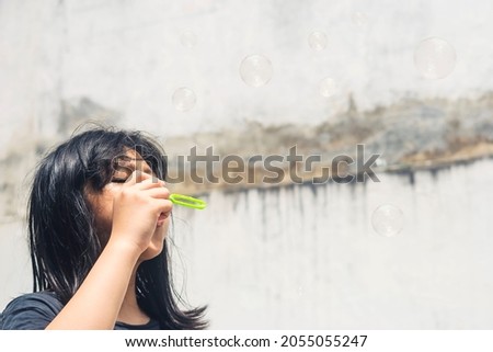A girl holding a bubble maker and blowing them out. Image focused on the girl.