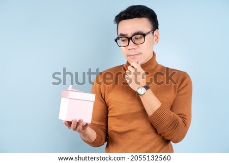 Asian man holding pink giftbox on blue background