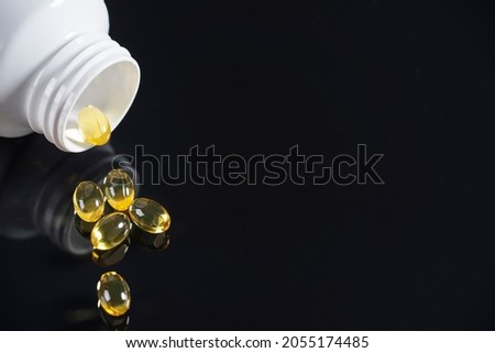 Pills and a white bottle of medicine lie on a mirrored black background, reflected in it.