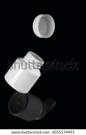 White bottle with medicine hang over a mirrored black background, reflected in it.