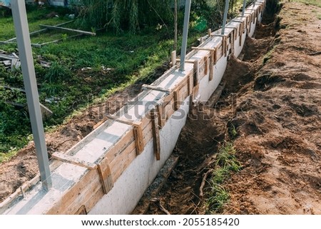 Timber formwork with metal reinforcement with pour concrete and creating a solid foundation for a building or fence. Construction process. Building the retaining wall. Side view. Nobody. Copy space. Royalty-Free Stock Photo #2055185420