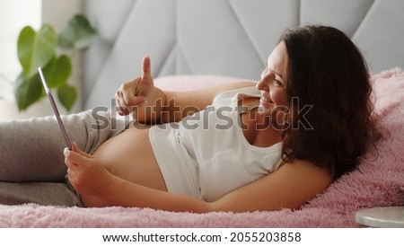 Happy pregnant woman expecting a baby lying on sofa with tablet,  at home. Pr