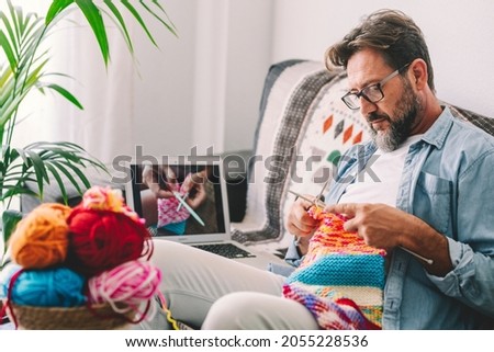 One adult man at home follow online knit tutorial to relax and enjoy resting home leisure activity sitting on the sofa - male people knitting with computer class help - people inner lifestyle hobby Royalty-Free Stock Photo #2055228536
