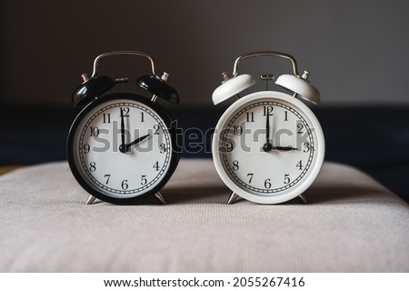 Two retro table clocks, black and white color, showing daylight saving time concept Royalty-Free Stock Photo #2055267416