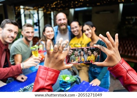 Female hands taking photo with mobile phone of young friends at trendy cocktail pub - Diverse millennial people posing for a picture while drinking together at open air bar - Focus on phone screen