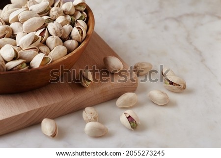 Tasty pistachio nuts in a wooden bowl on a wooden cutting board on a wooden table, side view. Close up