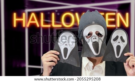 Scary ghost with two skull masks in hand isolated with neon halloween lights in the background.