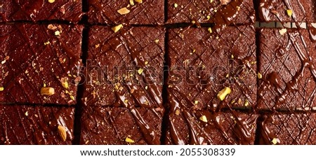Chocolate squares with pistachio nuts and strawberries on white paper on a light background, top view, horizontal composition. Banner.