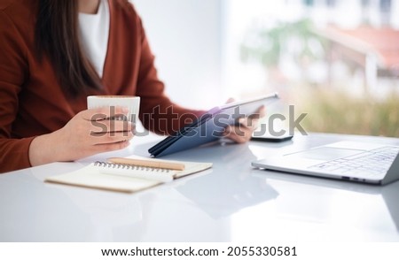 focus on hand young asian businesswoman using mobile app from digital tablet working and meeting online and other hand holding coffee cup