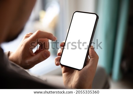 Man using smartphone blank screen frameless modern design while sitting on the chair in home interior