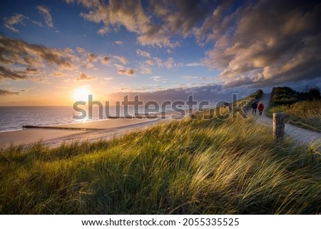 two people walking along the coastal path at sunset at the Zeeland coast near Zoutelande Royalty-Free Stock Photo #2055335525