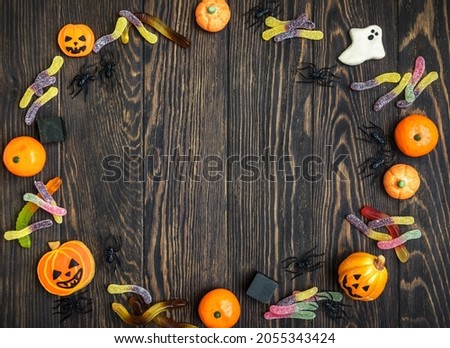 Halloween background with cookies, flat lay. Food on wooden vintage table for Hallowen celebration. Frame of Helloween sweets. Top view of Halloween ghost, pumpkin and worms on dark textured boards.