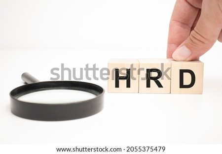 hrd text wooden cube blocks and hand holding magnifying glass on table background.